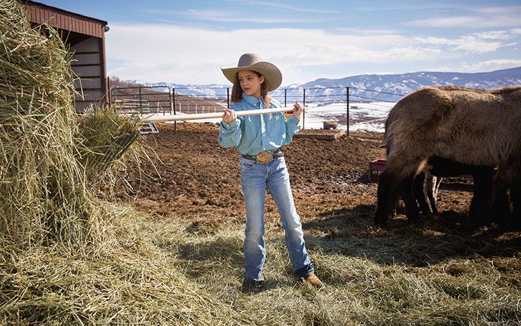 La niña usa una horca para obtener heno para alimentar a los caballos y al ganado.